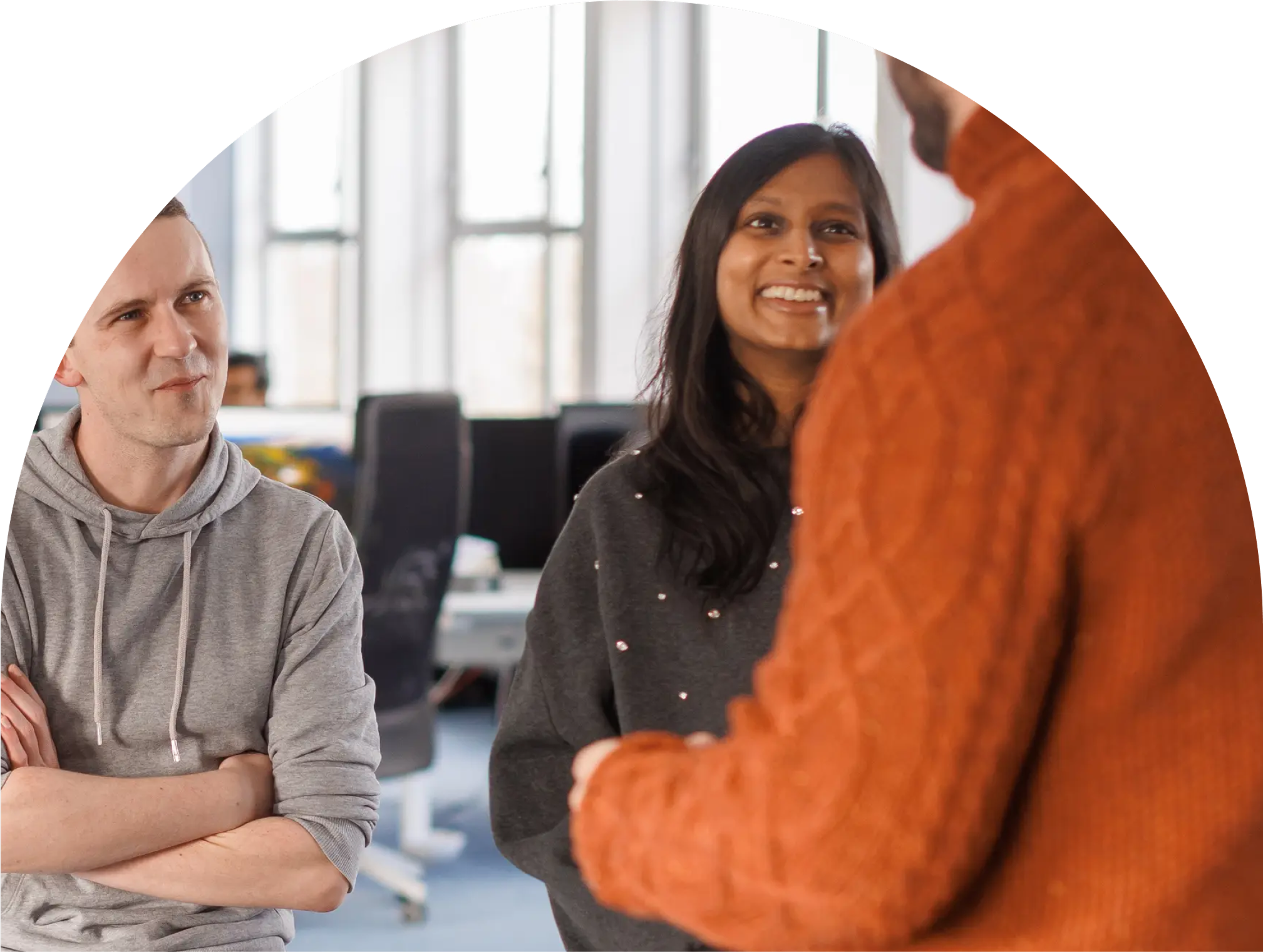 Three people engaged in a friendly conversation in a brightly lit modern office.