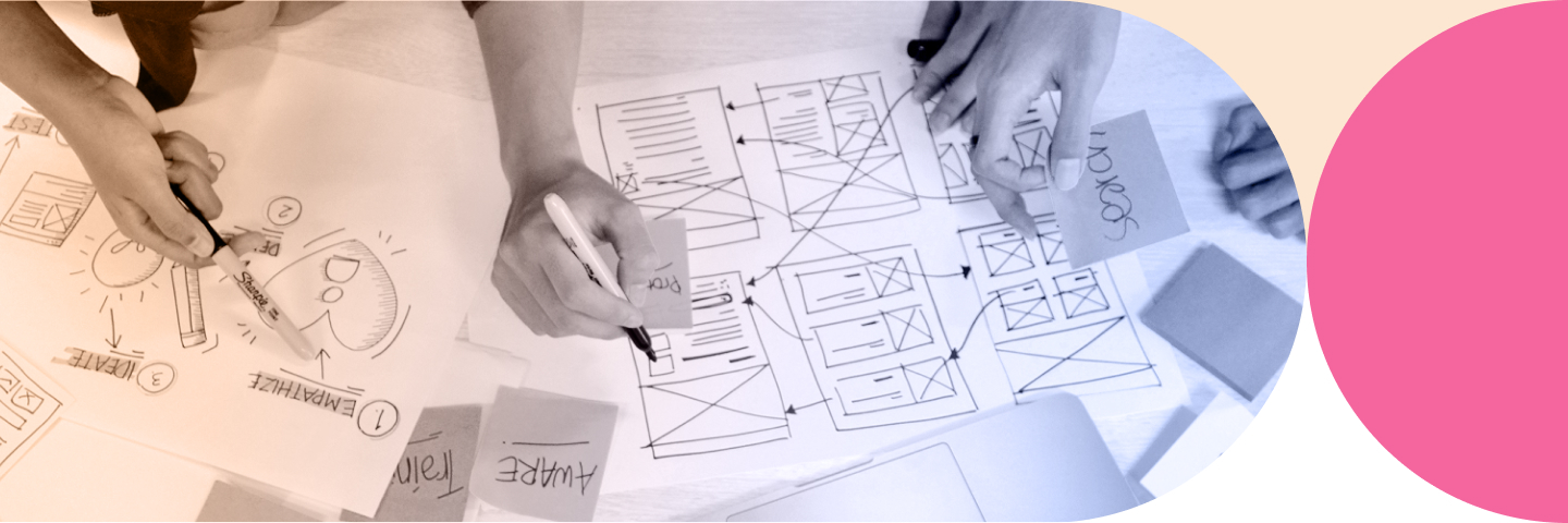 Hands sketching website wireframes and flowcharts on paper with markers and sticky notes.