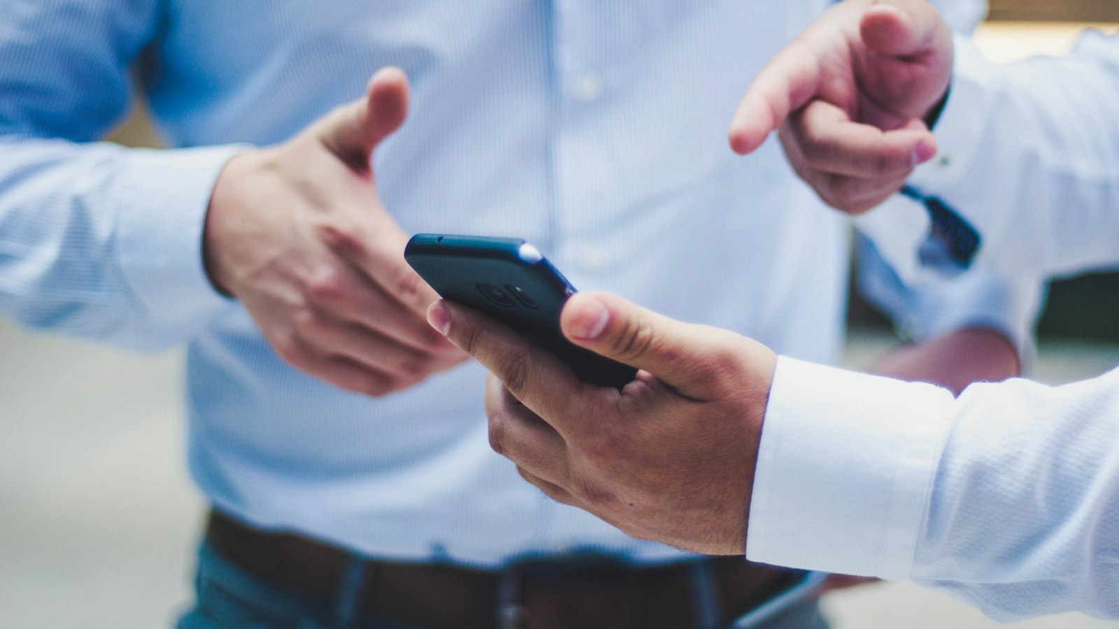 Deux mains autour d’un smartphone, en chemise blanche