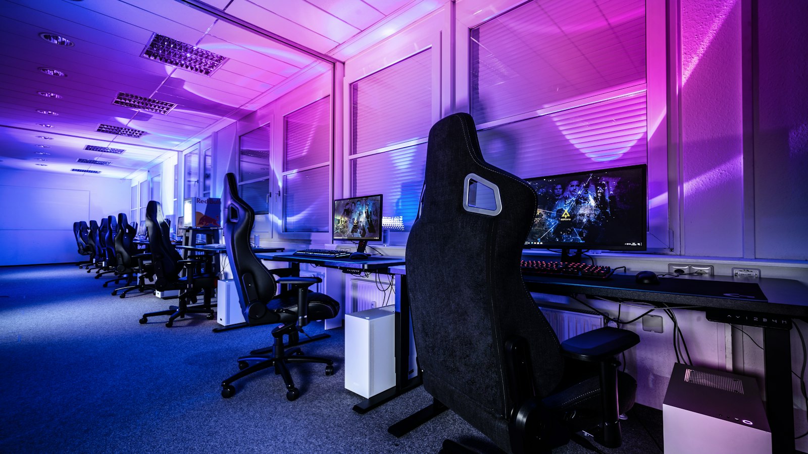 Salle de jeu vidéo éclairée en bleu et violet, avec des postes alignés