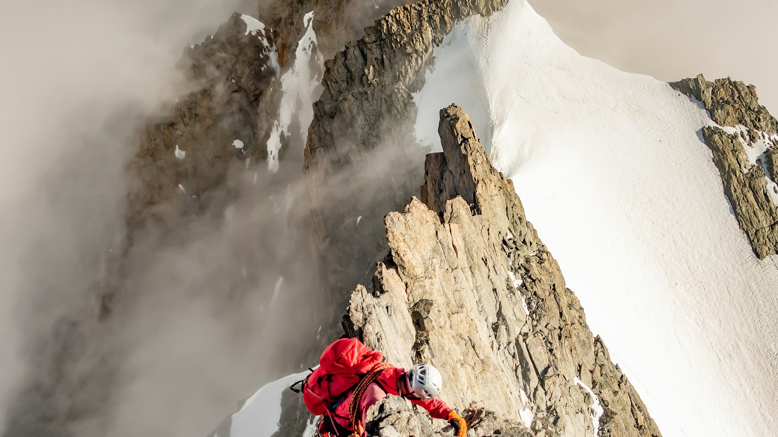 Alpiniste en veste rouge sur une crête rocheuse enneigée