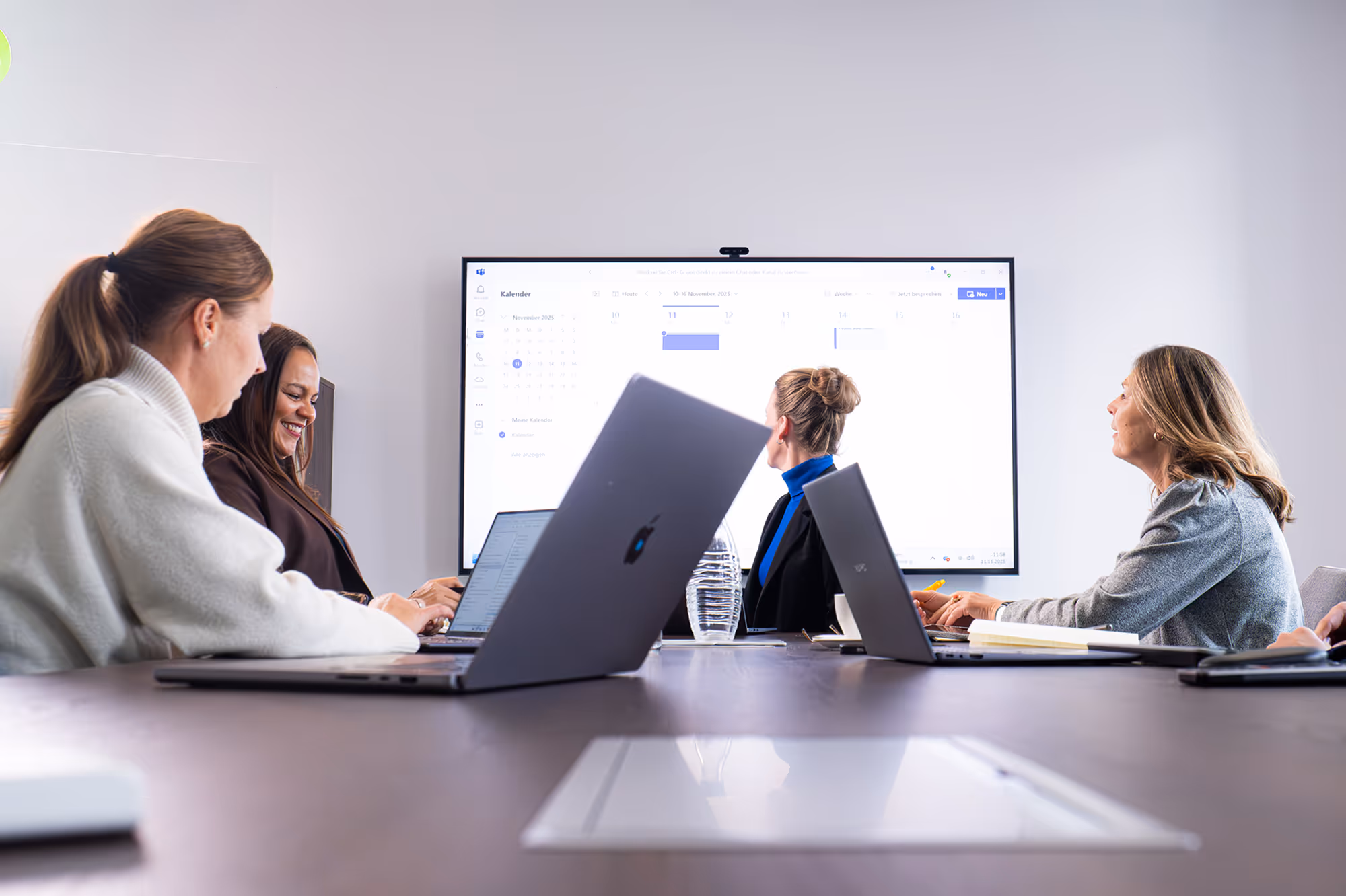 Mehrere NUE Mitarbeitende sitzen an einem Konferenztisch mit Laptops und blicken auf einen großen Bildschirm mit Präsentationsinhalten.
