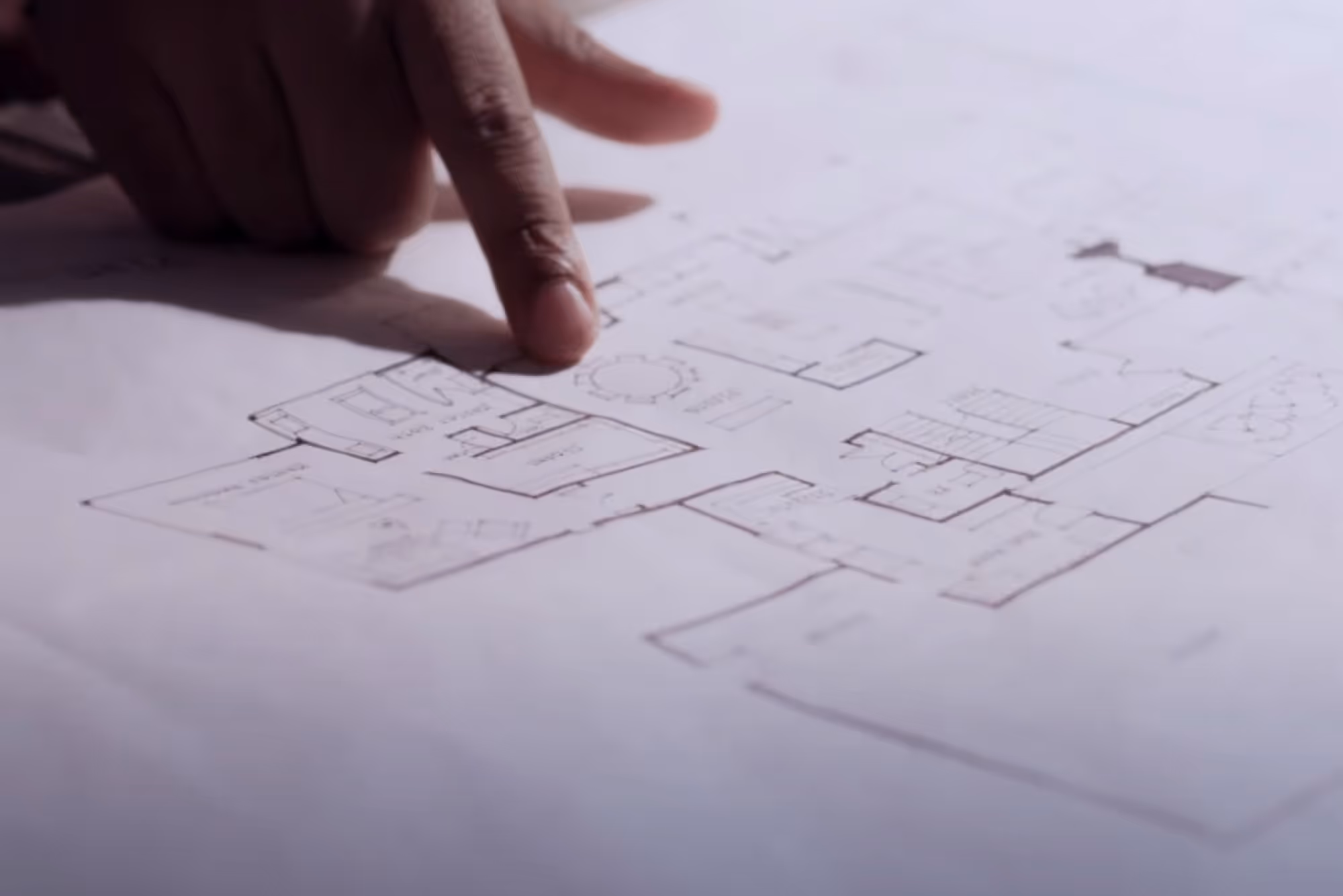 Eine Hand zeigt auf die Skizze eines architektonischen Grundrisses auf weißem Papier.