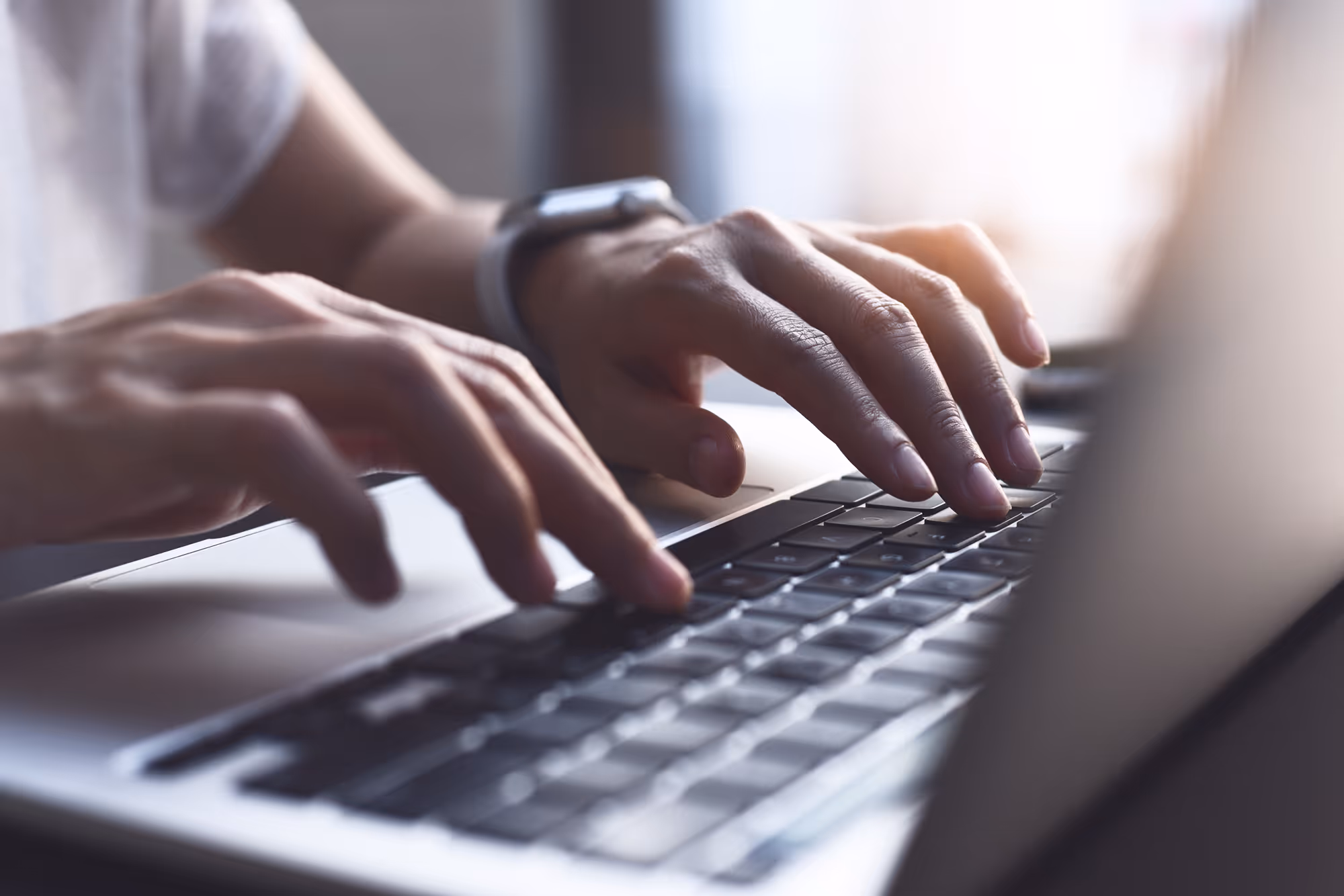 Hände tippen auf einer Laptop-Tastatur mit unscharfem Hintergrund.