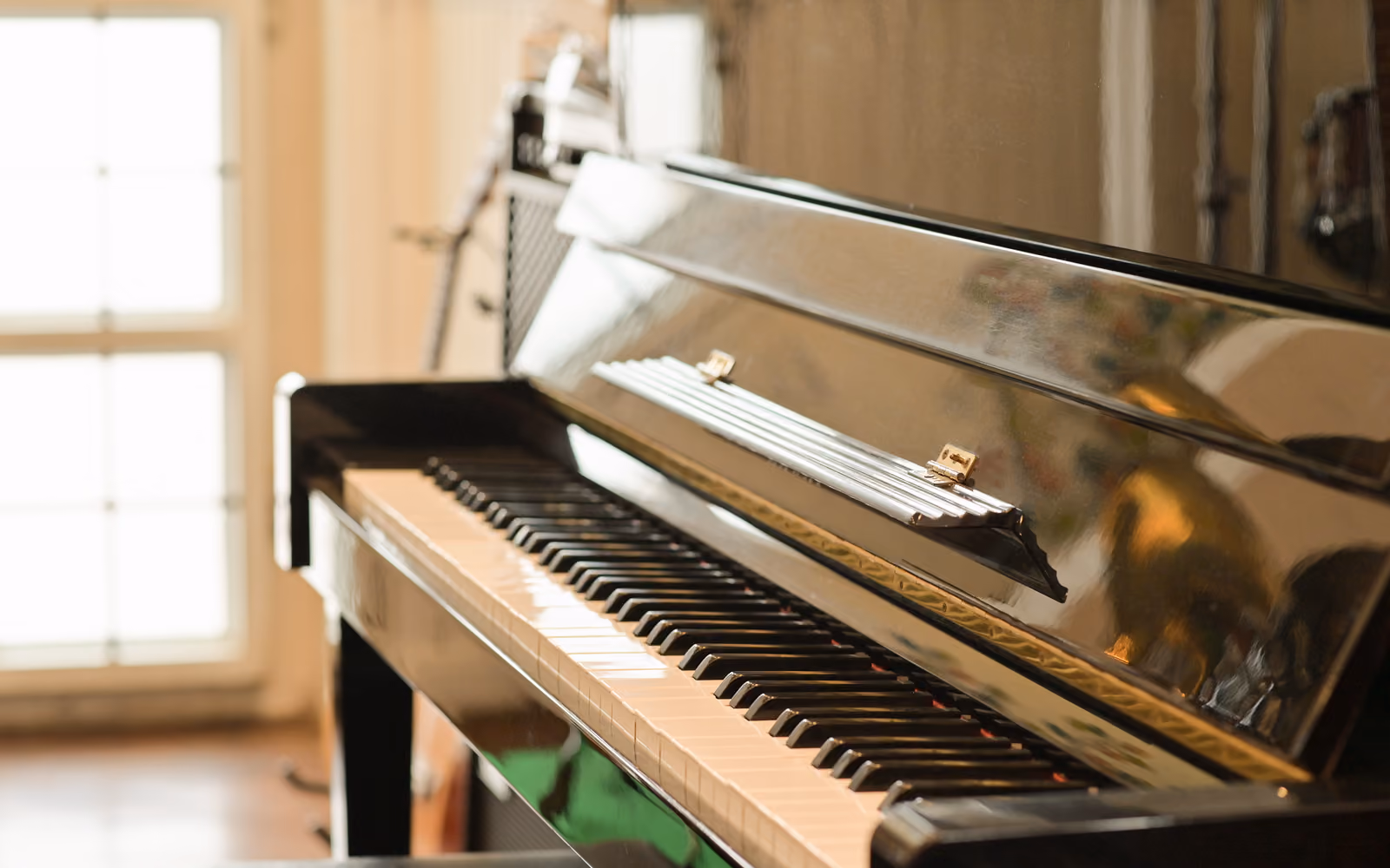 Schwarzes Klavier mit sichtbarer Tastatur vor einem Fenster.