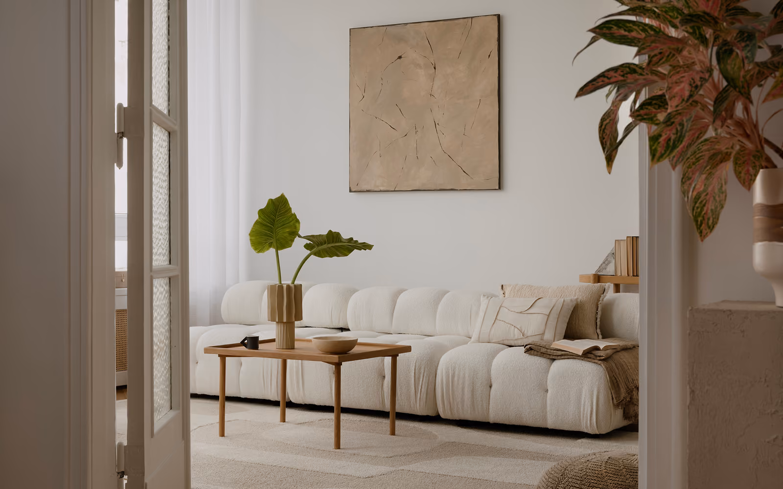 Helles Wohnzimmer mit cremefarbenem Sofa, Holztisch, Zimmerpflanzen und einem Bild an der Wand.