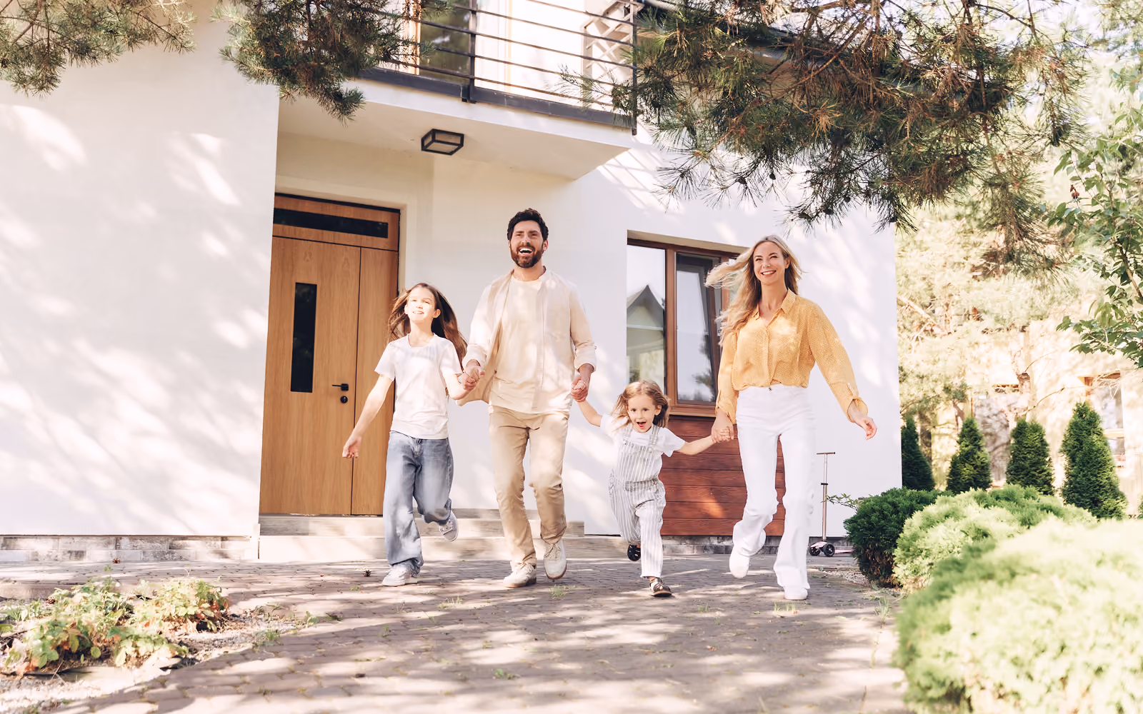 Eine Familie mit zwei Kindern läuft Hand in Hand auf der Einfahrt vor ihrem Haus.