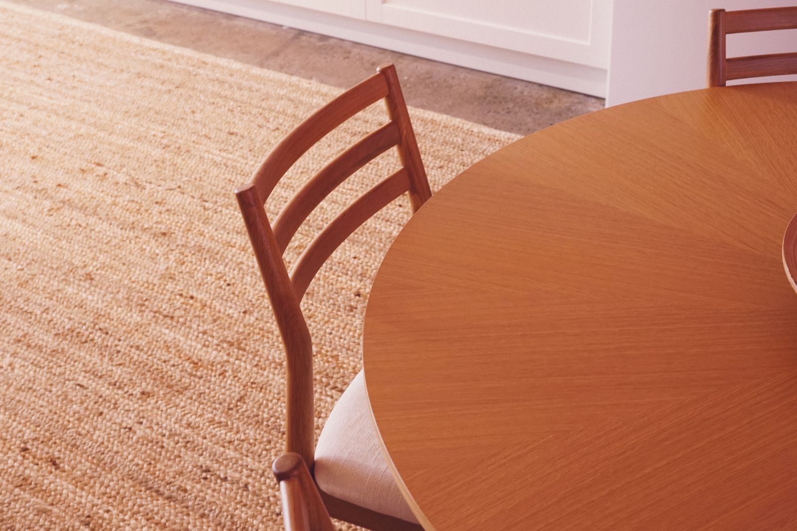 Close-up of a wooden round dining table with a wooden chair featuring a cushioned seat beside it on a woven beige rug.
