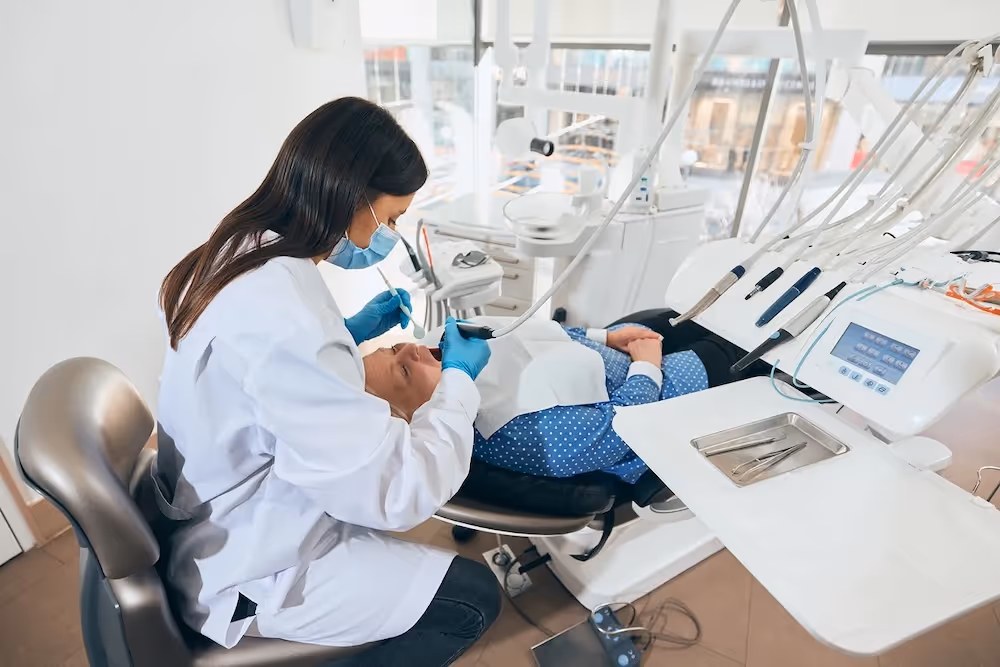 Dentist in white coat and mask treating a patient reclining in a dental chair.
