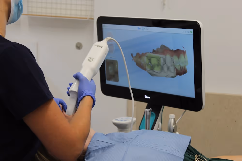 Dental professional wearing gloves using an intraoral scanner to capture a digital 3D image of a patient's teeth on a screen.