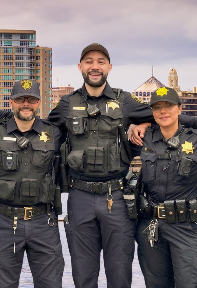 Four female police officers in blue uniforms smiling and standing close together outdoors.