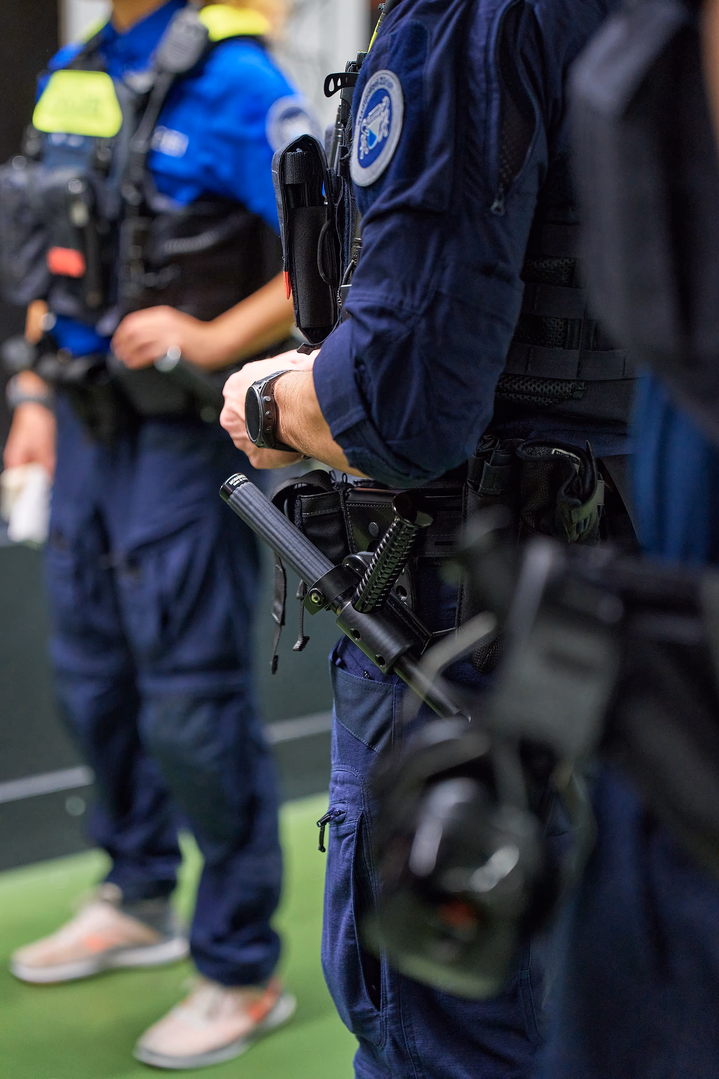 Polizisten in blauen Uniformen bei einem Schießtraining, Fokus auf Ausrüstung und Taser am Gürtel eines Polizisten.