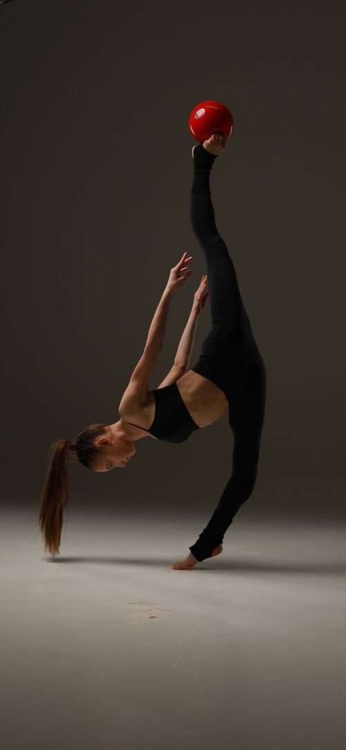 Rhythmic gymnast practicing a ball balance in a dark studio
