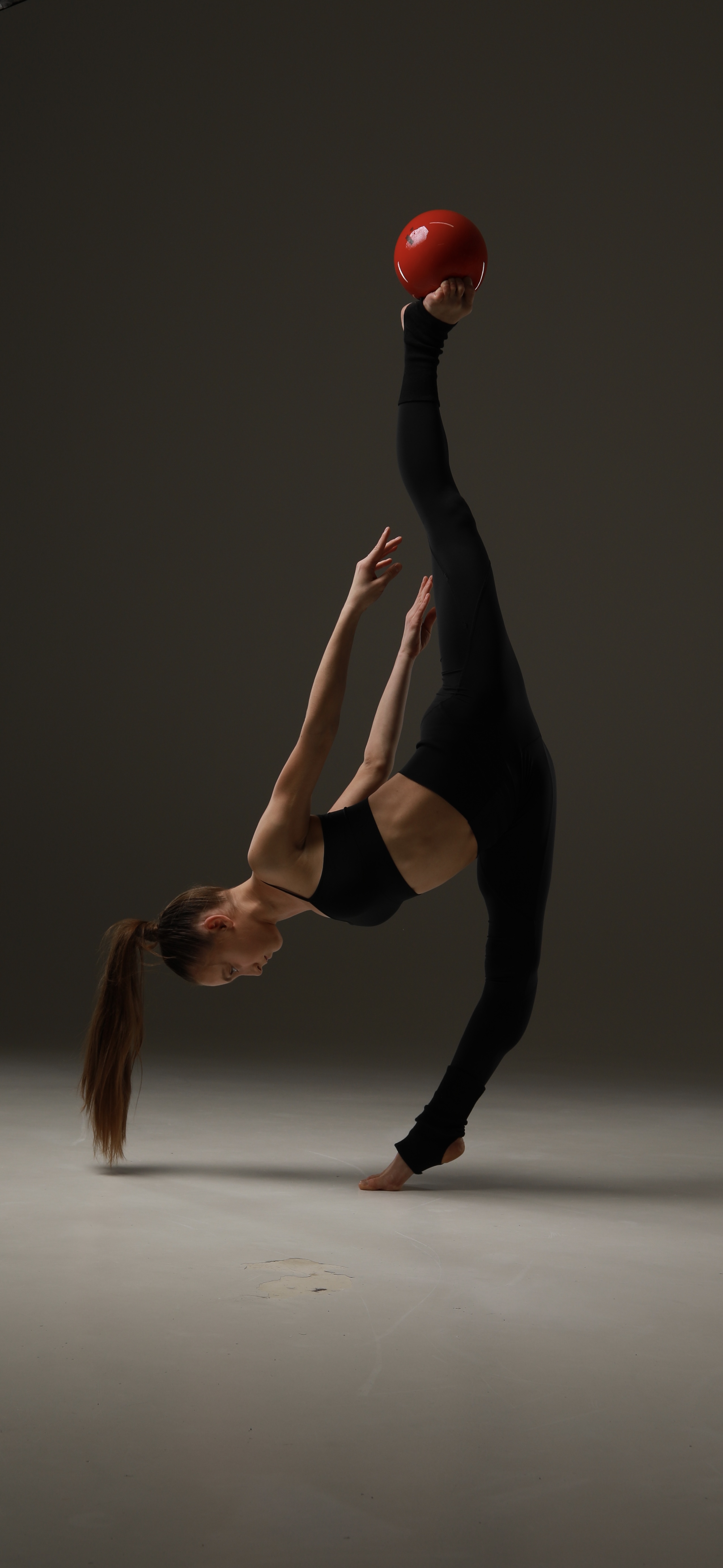 Rhythmic gymnast practicing a ball balance in a dark studio