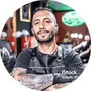 Tätowierter Friseur mit verschränkten Armen posiert in einem stylischen Barbershop.