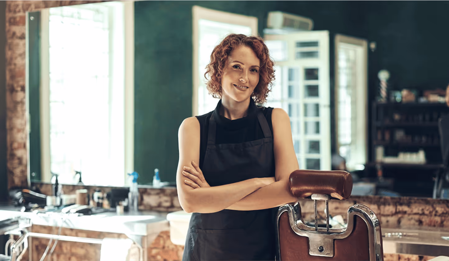 Selbstbewusste Friseurin mit verschränkten Armen in einem modernen Salon.