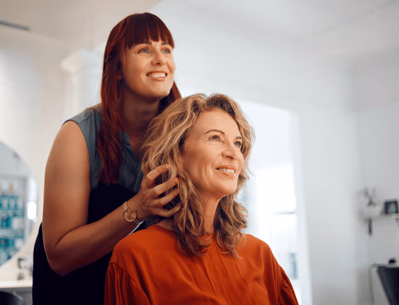 Zwei Friseurinnen frisieren und beraten eine glückliche Kundin.
