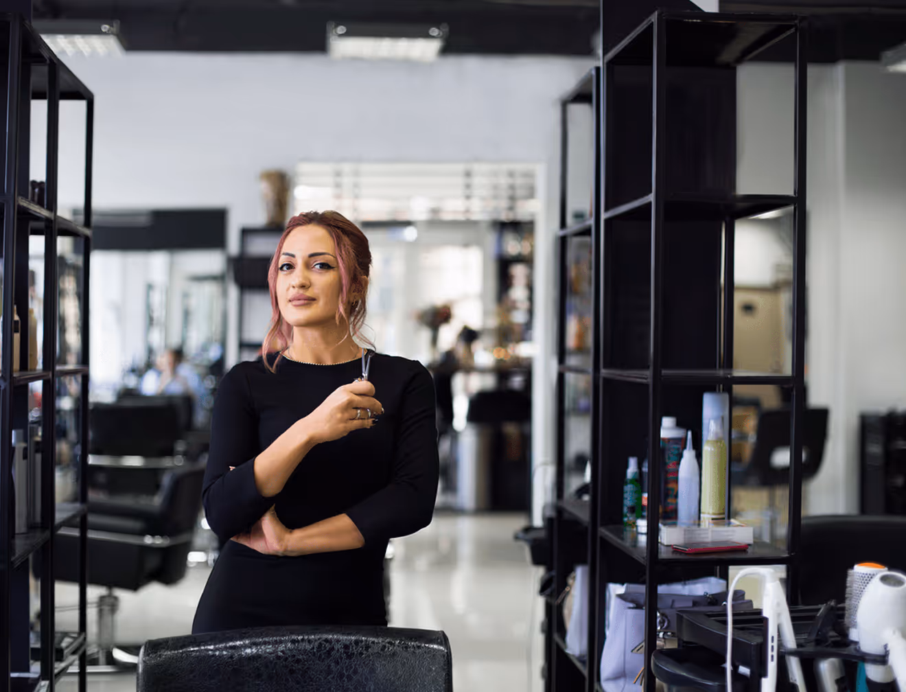 Friseurin steht mit verschränkten Armen selbstbewusst in einem modernen Friseursalon.