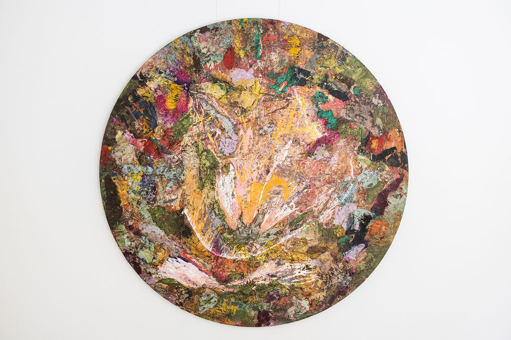 Round abstract painting featuring a vibrant mix of textured colors including yellow, green, red, purple, and white.