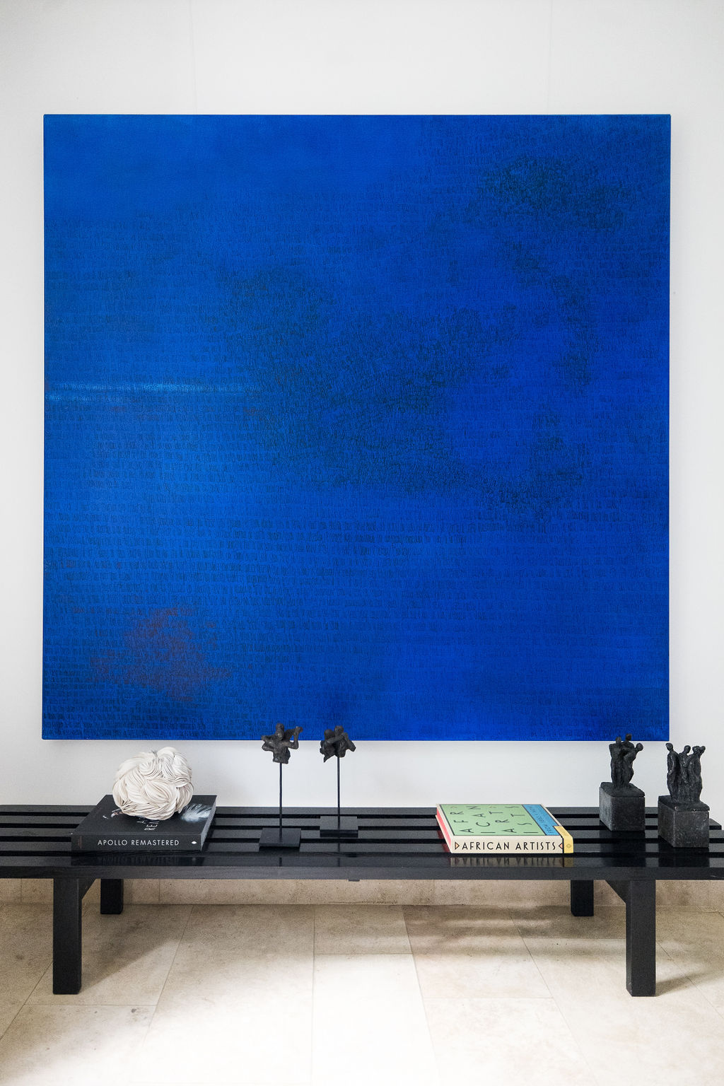 Charlotte Vindevoghel — Deep blue abstract painting above a black bench with small objects.