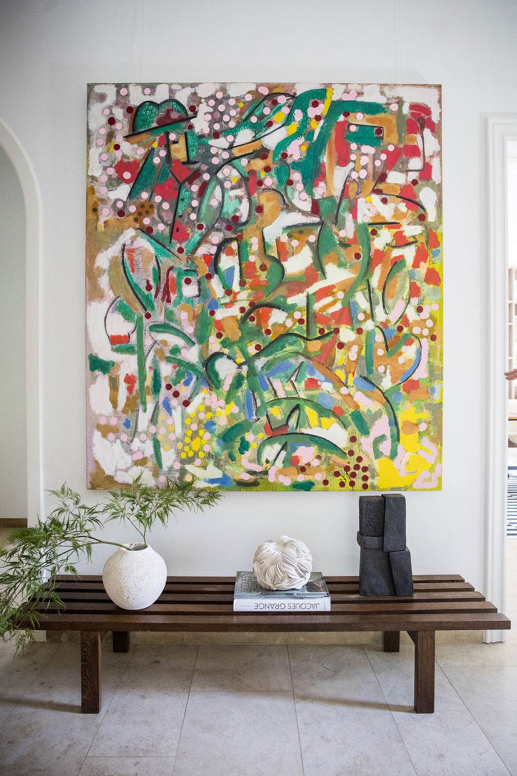 Manuel Esnoz — Colorful abstract painting above a slatted bench with books and a plant.