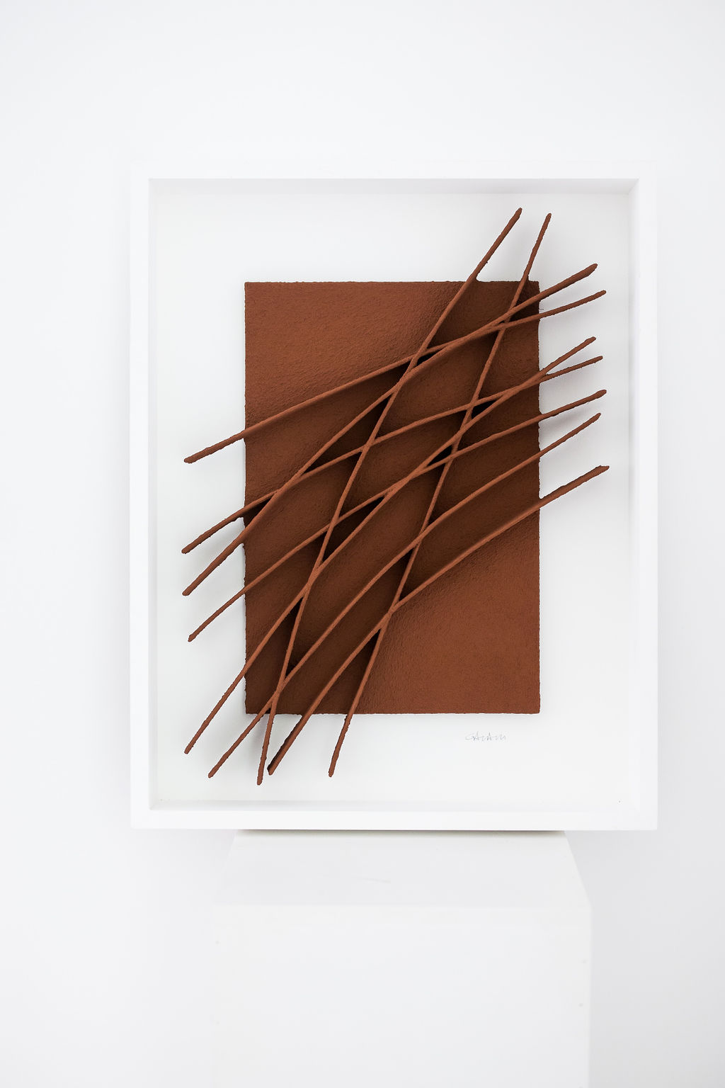 René Galassi — Terracotta relief with diagonal rods in a white frame on a pedestal.