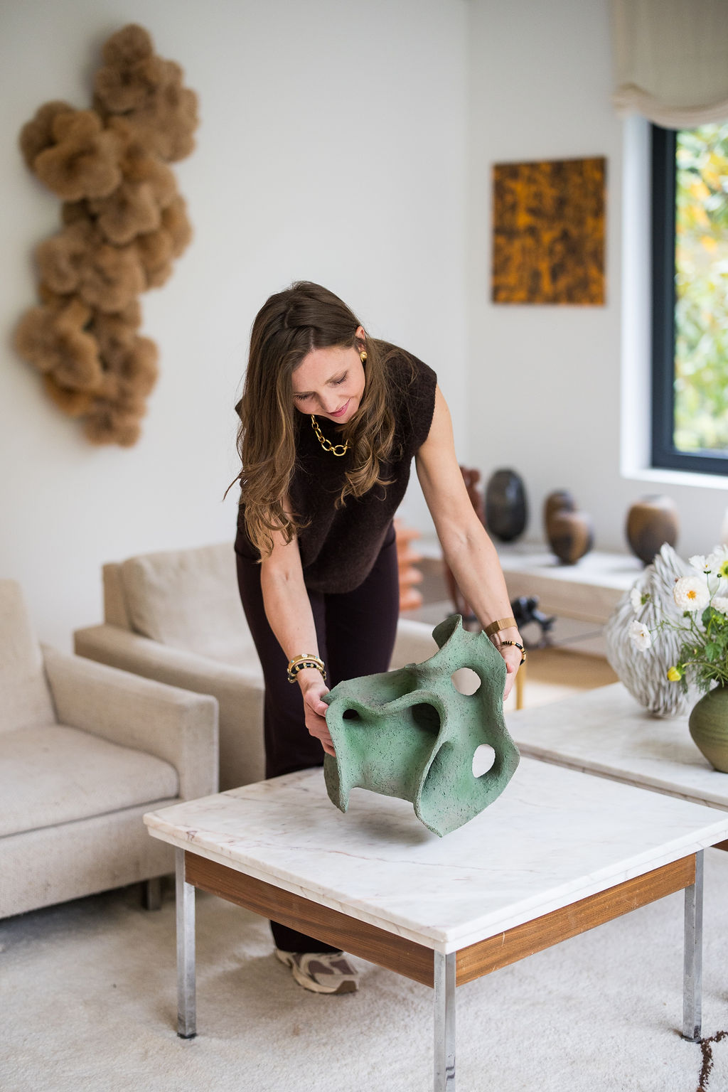 Green contemporary ceramic sculpture by Belgian artist Liliane Demeester being positioned on a marble table in a curated interior.