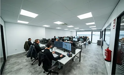 Modern office with multiple employees working on desktop computers at long white desks.