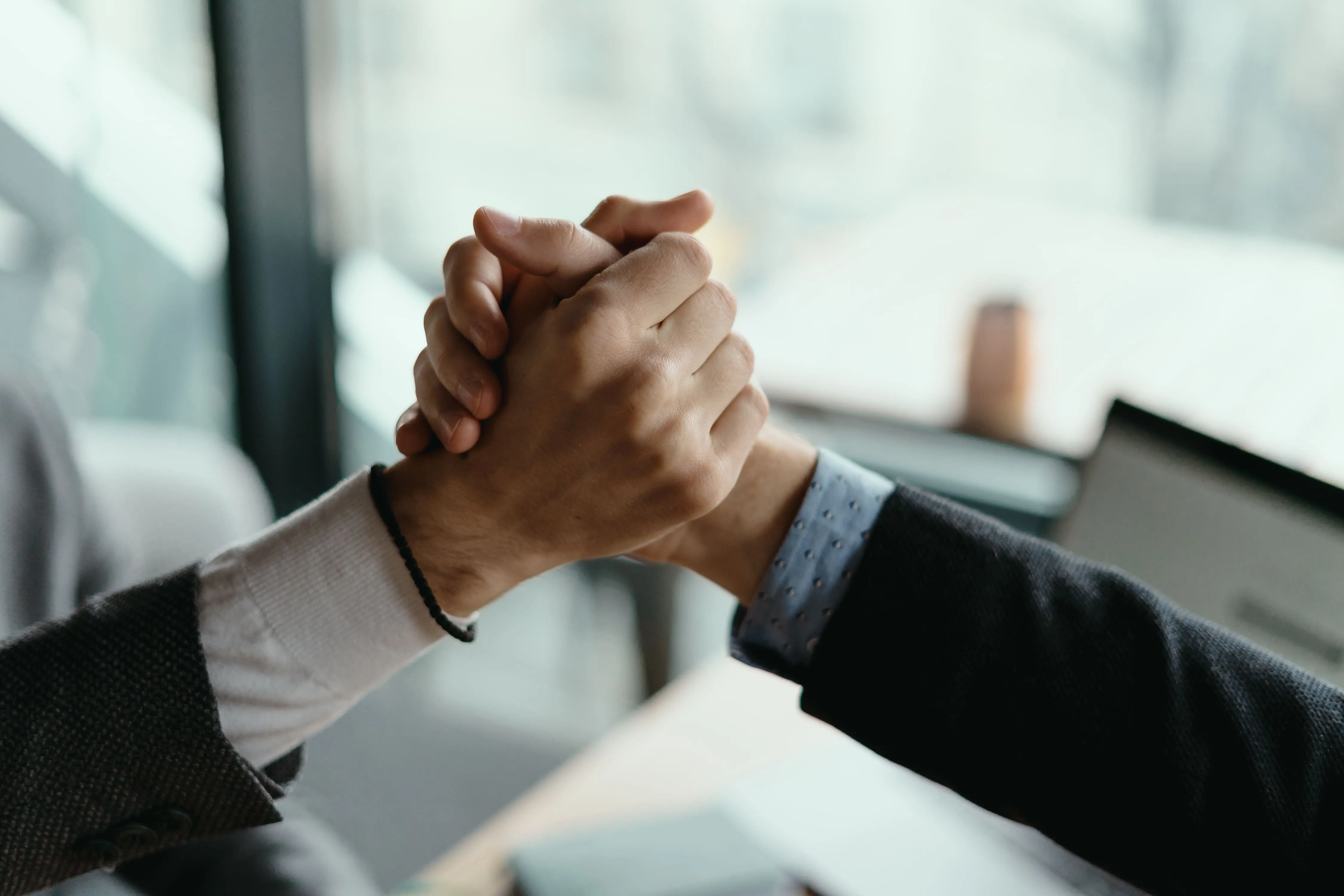 Two people clasping hands in a firm handshake indoors, suggesting agreement or partnership.