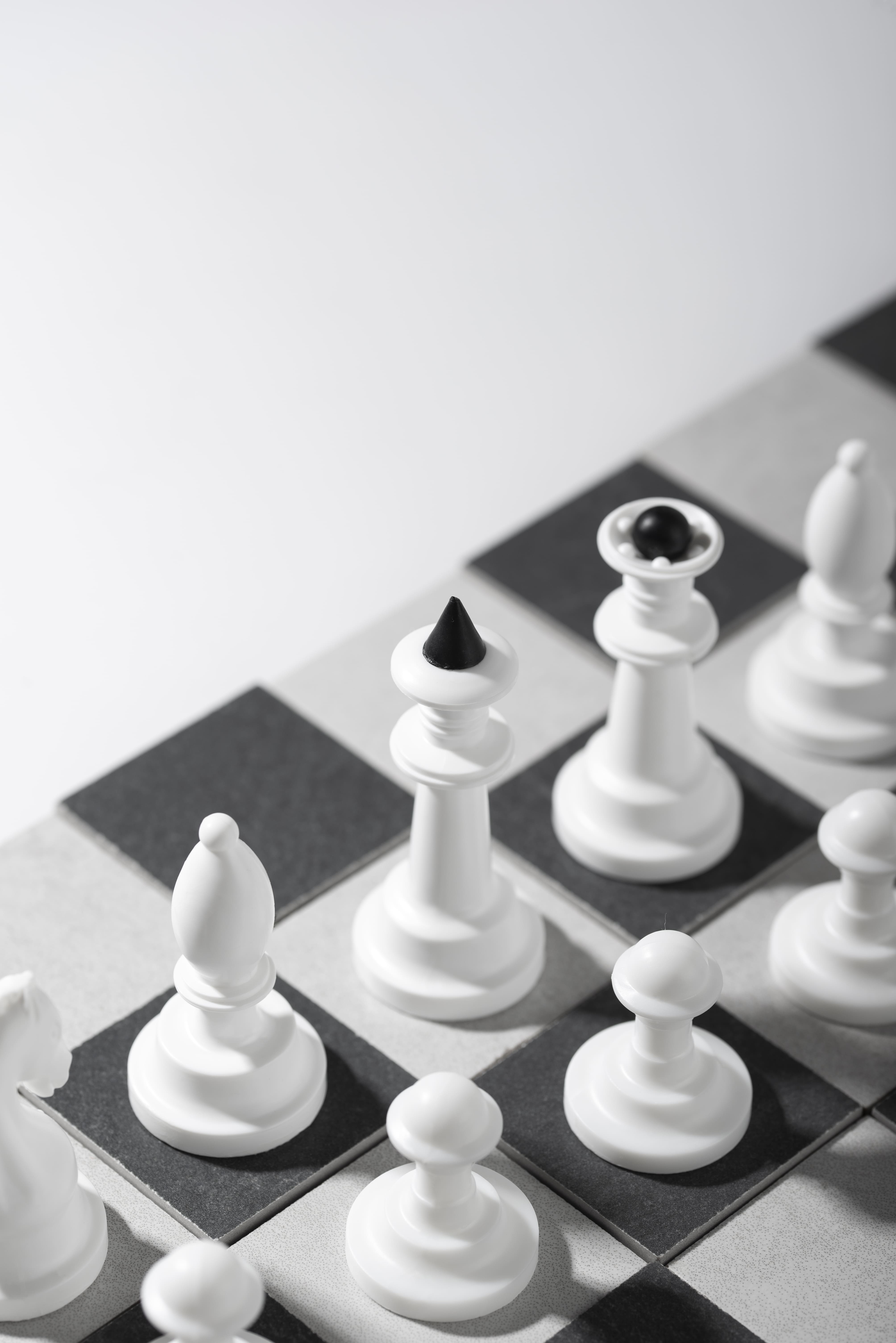 White chess pieces on black and white chessboard squares with a white queen topped by a black cone.