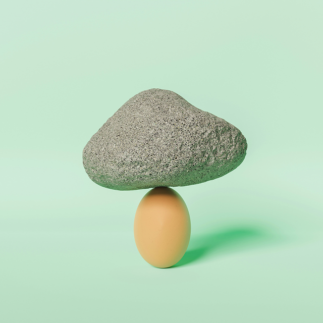 A large gray rock balanced on top of a brown egg against a light green background.