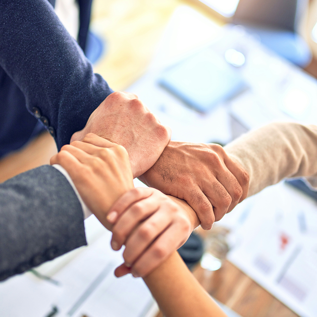 Four hands joined together in a collaborative gesture over a desk with office documents.