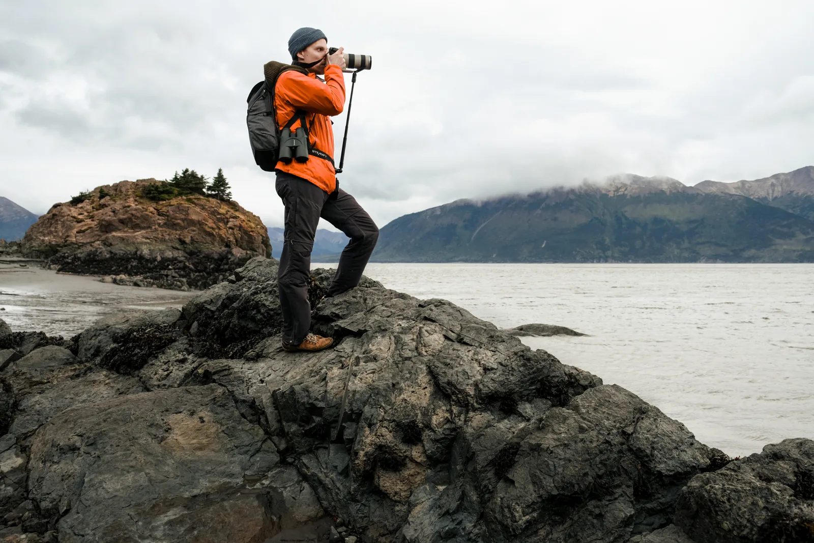 Photographer on coastal rocks holding a heavy lens supported by Steadify