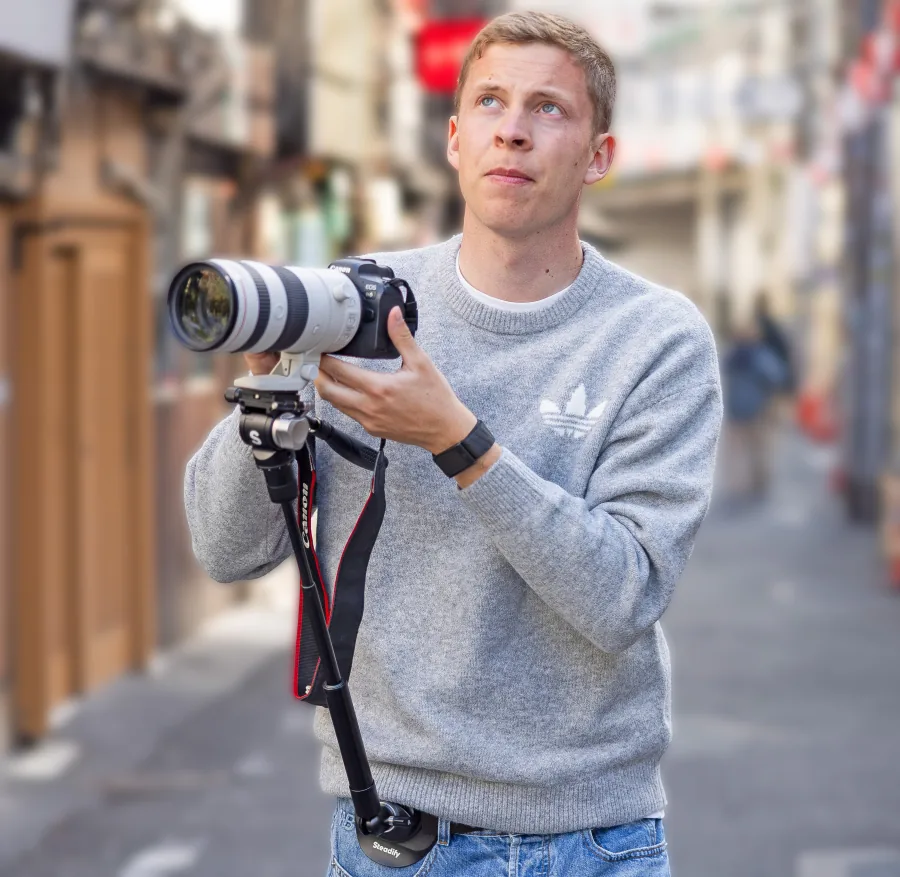 Portrait of travel photographer Tobias Bruns holding a camera on a city street