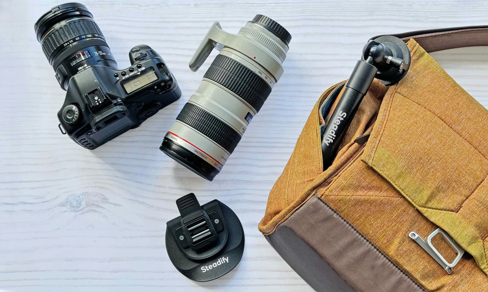 Camera, telephoto lens and folded Steadify laid out beside a shoulder bag