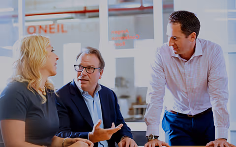 An image of three William O'Neil team members have a meeting in a glass conference room.