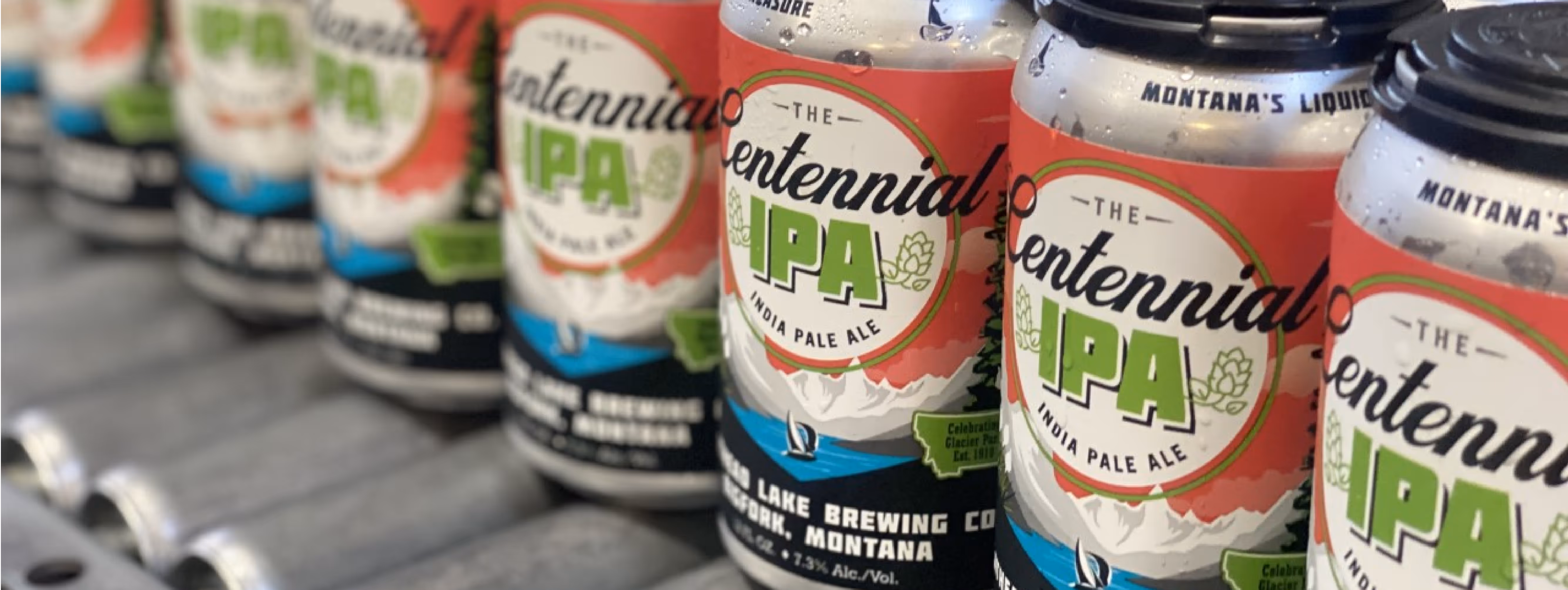 Cans of Centennial IPA with colorful labels featuring green text and red and white accents are lined up diagonally on a conveyor belt in a brewery.