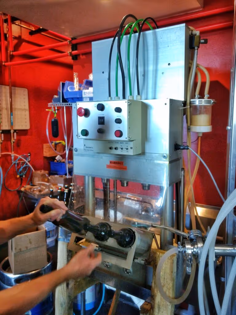 A person is filling bottles with beer, using a machine.