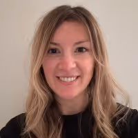 Smiling woman with long blonde hair wearing a black top against a plain light background.