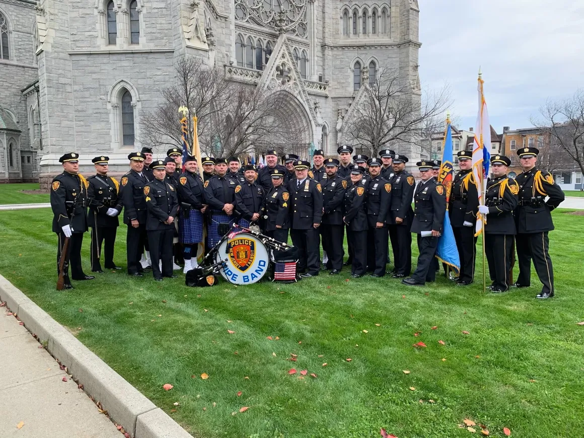 Members of the New Jersey Transit Police and Pipe Band pose together on a church lawn during a formal ceremony.