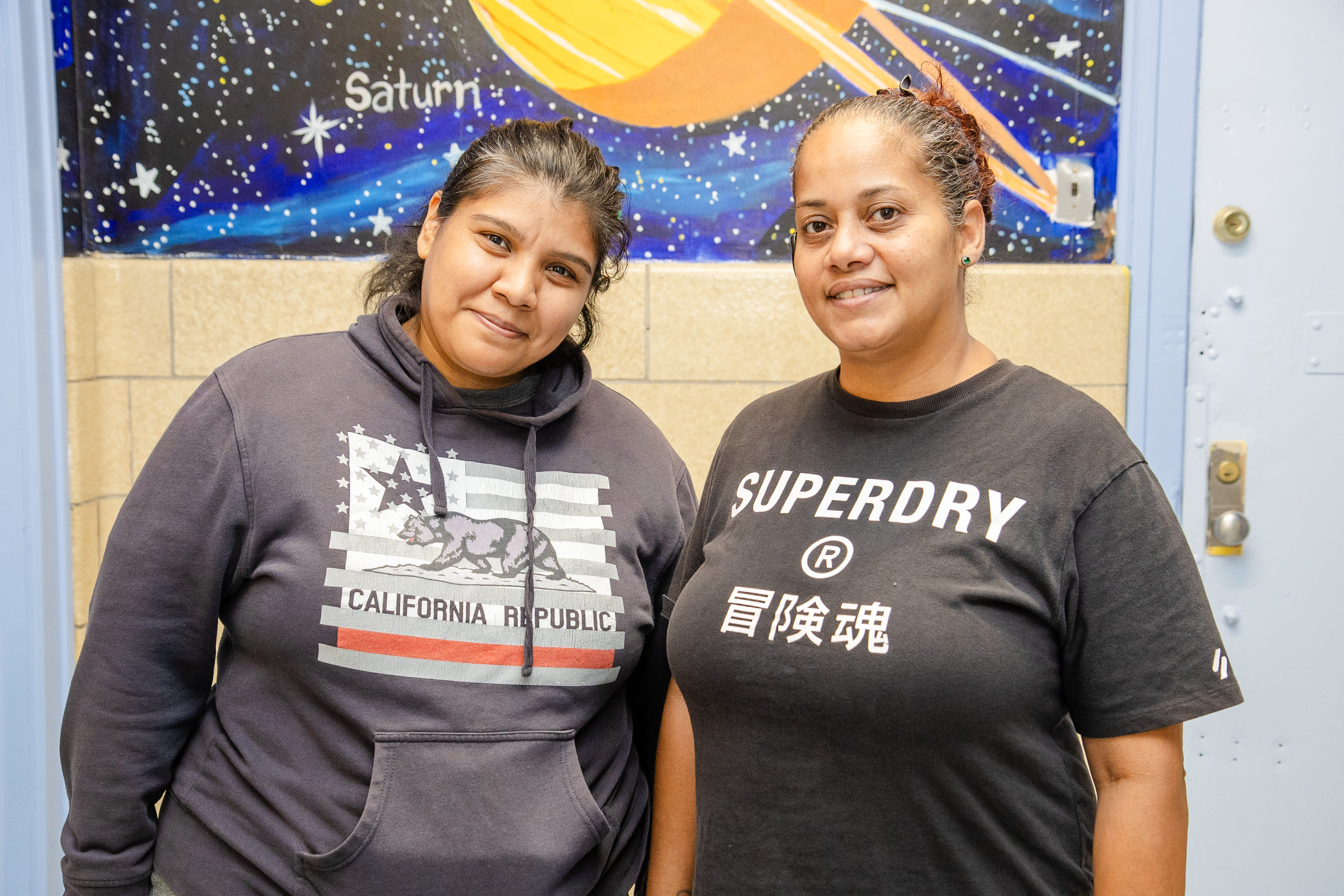 Two smiling staff members posing in front of student space mural