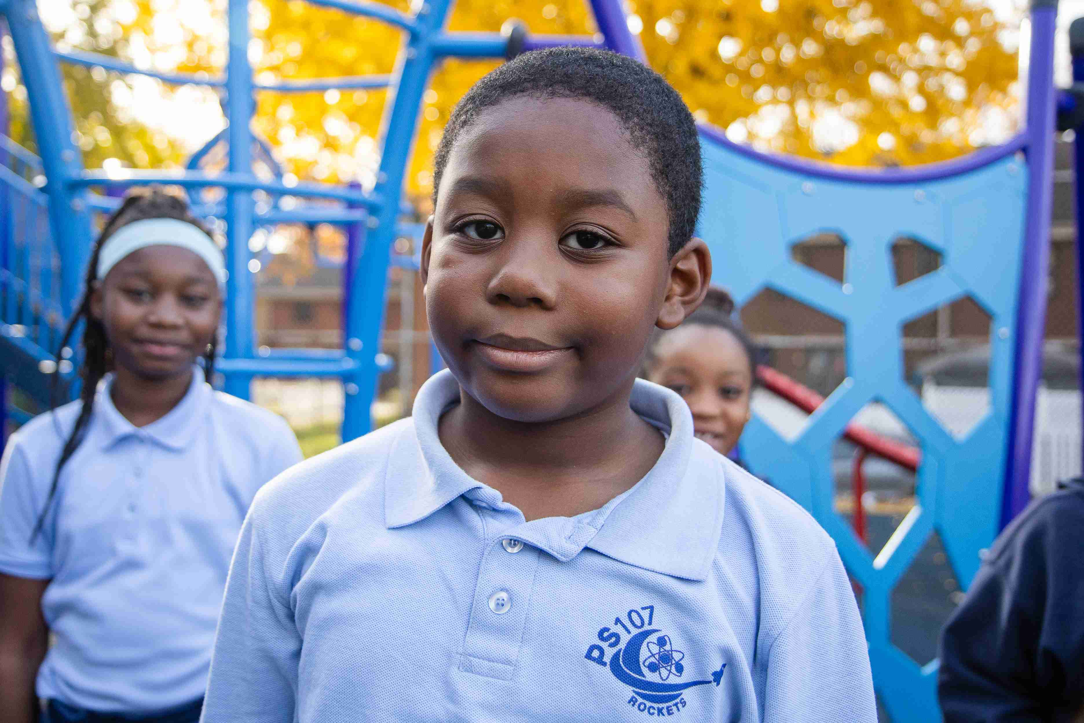 PS 107 Rockets student smiling on school playground with classmates