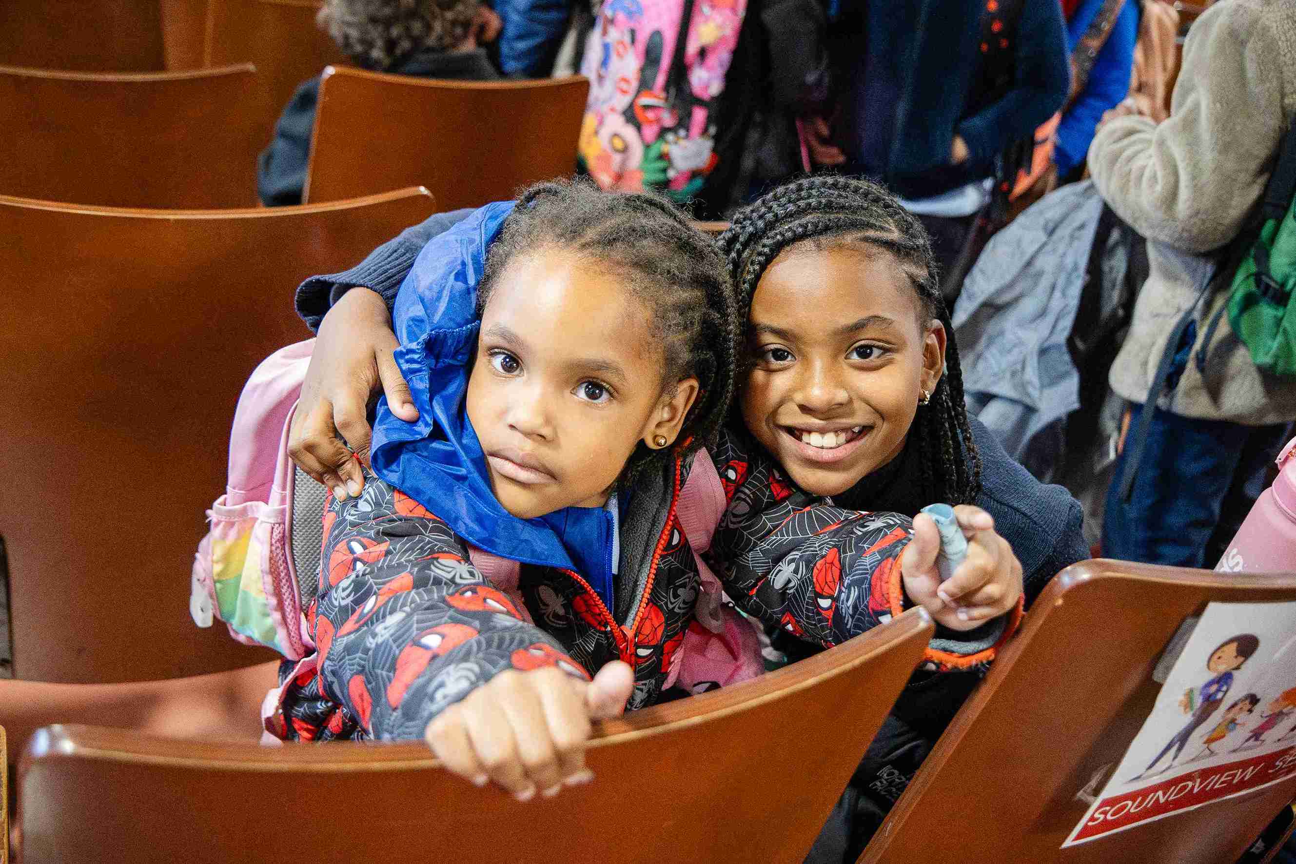 Two smiling students seated together at a school assembly