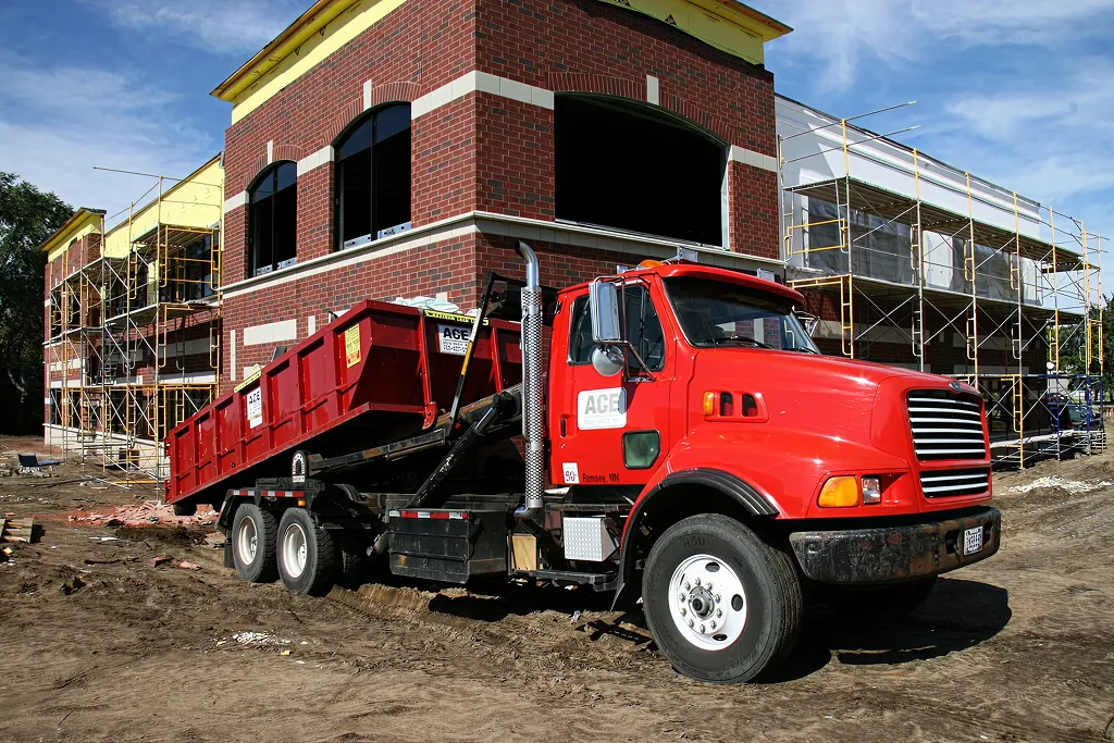 Red dumpster truck parked in front of a brick building under construction with scaffolding around it.