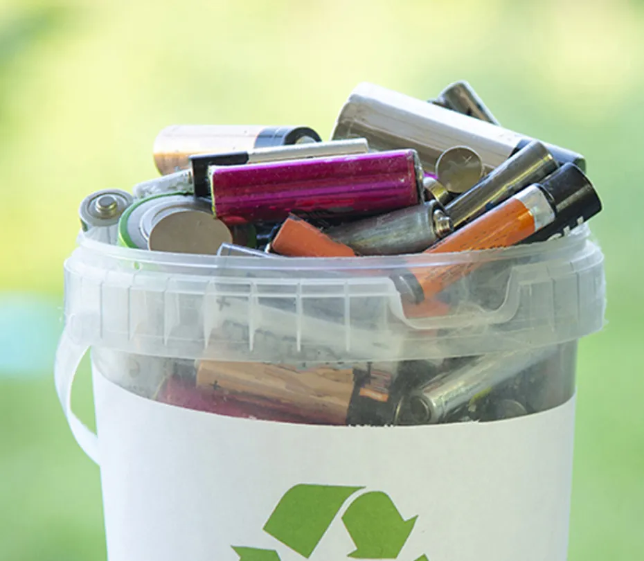 Plastic container filled with used batteries for recycling against green background.