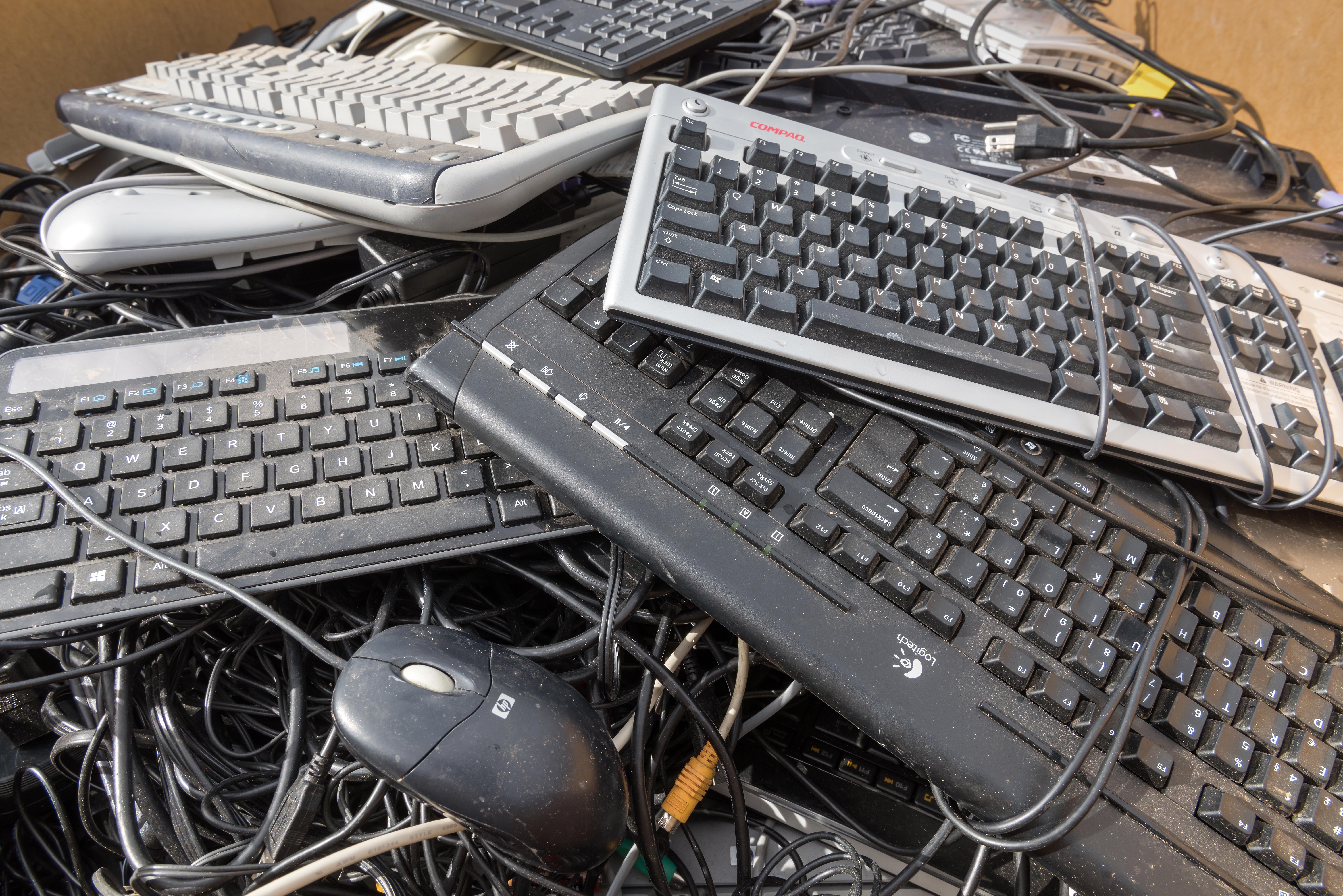 Pile of used computer keyboards, a mouse, and tangled cables representing electronic waste.