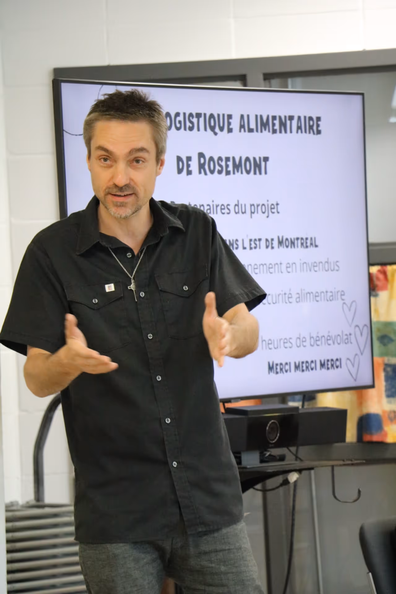 Un homme en chemise noire fait une présentation devant un écran affichant des informations sur la logistique alimentaire de Rosemont.