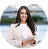 Smiling woman with long dark hair wearing a white blouse standing against a blurred outdoor background.