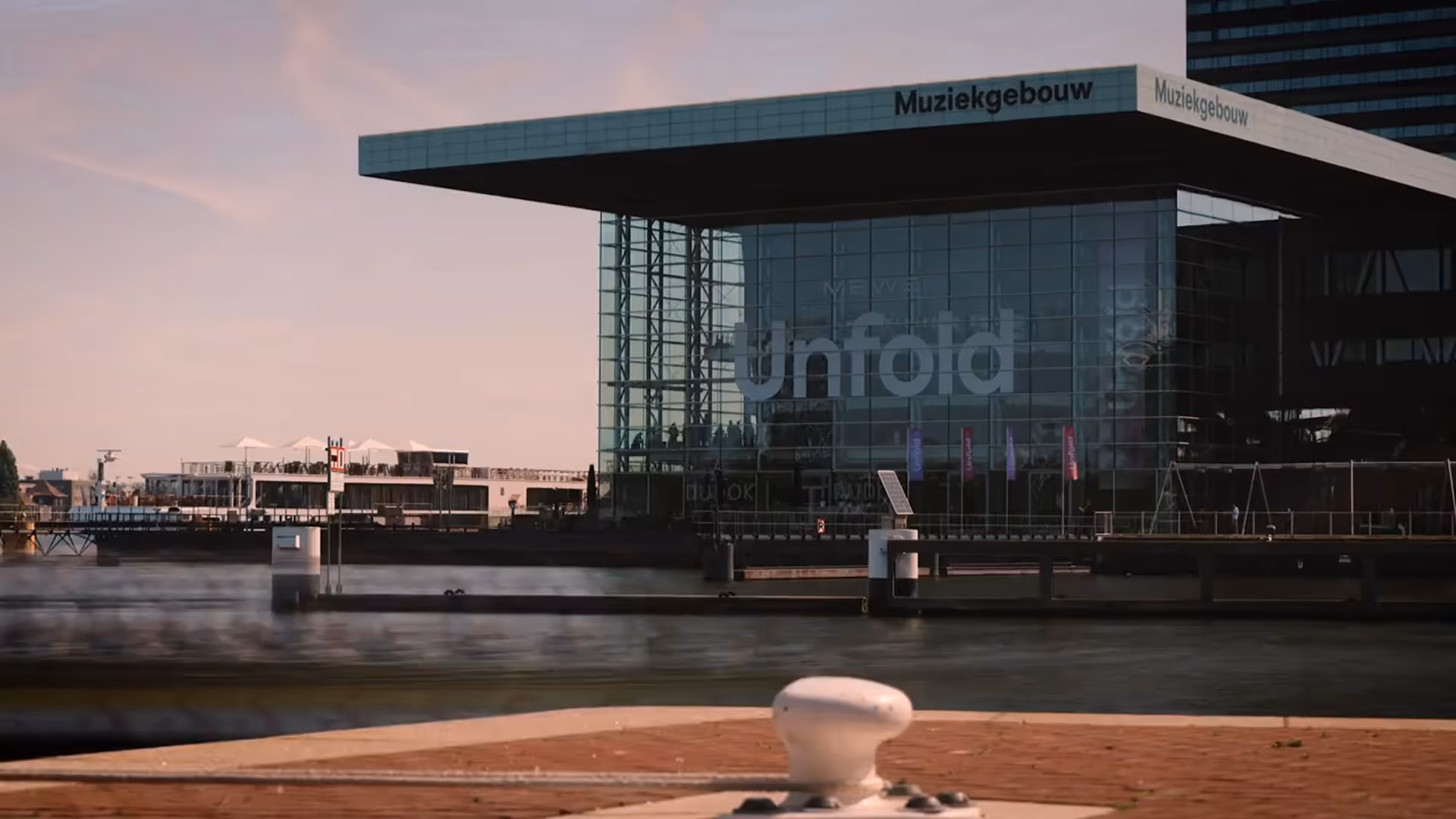 View of the Muziekgebouw concert hall with glass walls by the waterfront during sunset.