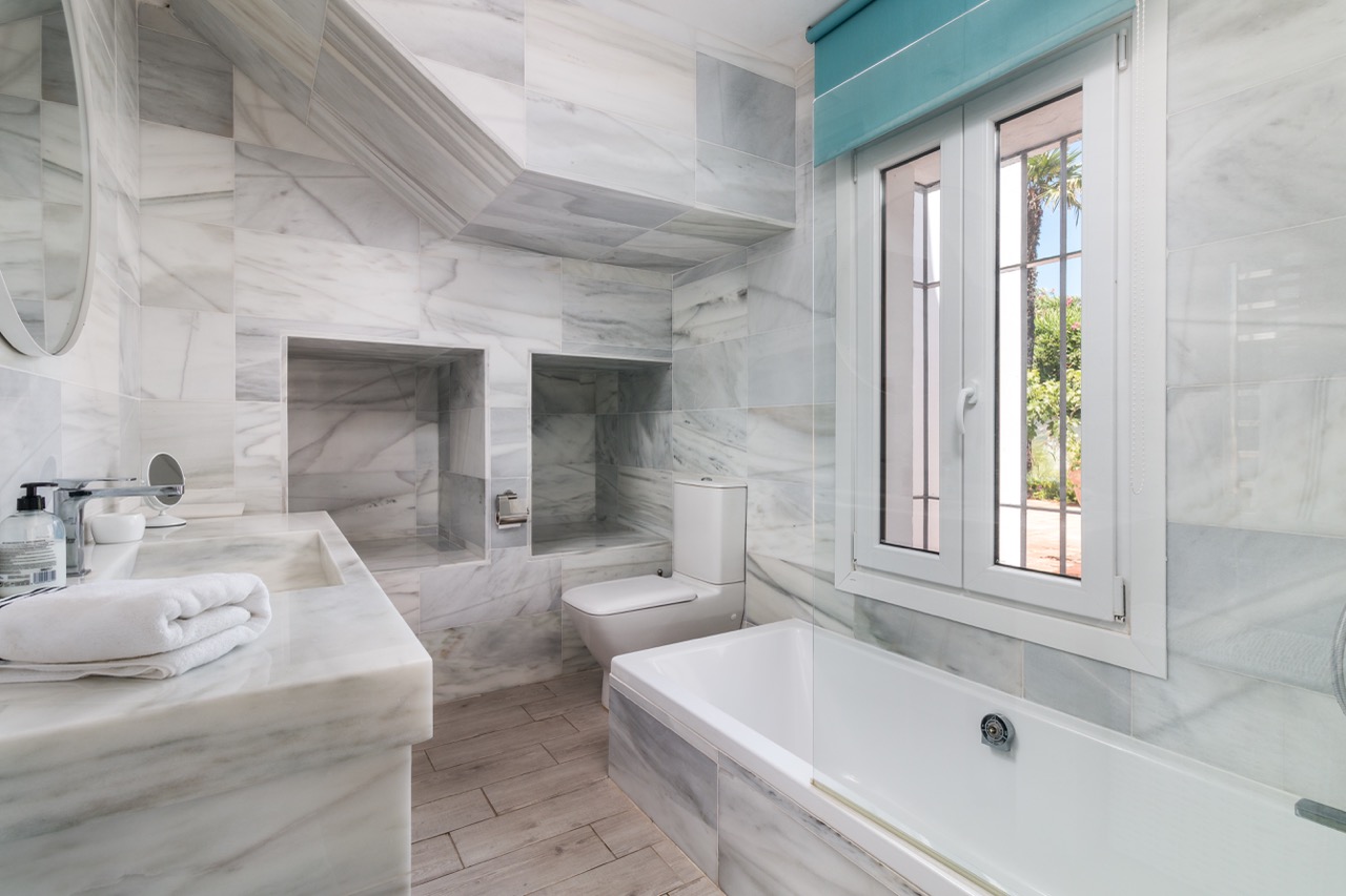 Baño con bañera, mueble de lavabo y paredes alicatadas efecto mármol